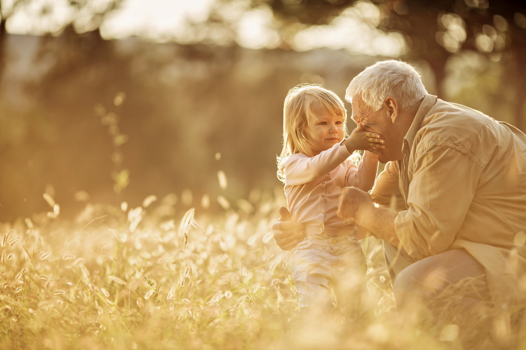 Young girl gently touching her grandfather's face in a meadow